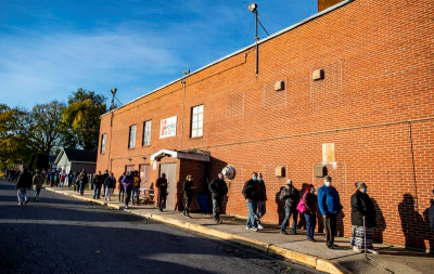 citizens line up to vote outside of a red brick building